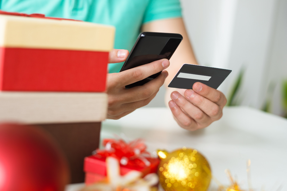 Closeup of Man With Credit Card, Smartphone and Christmas Gifts