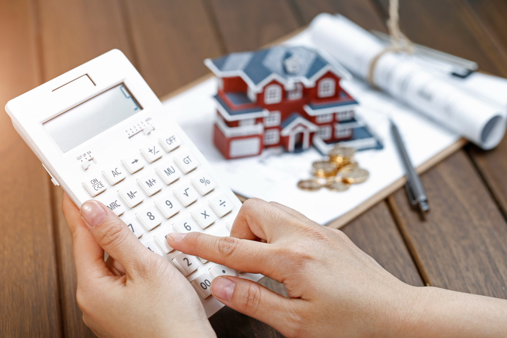 A Female Hand Operating a Calculator in Front of a Villa House Model