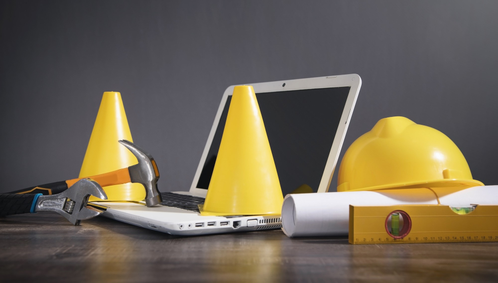 Yellow Traffic Cone, Helmet, Document, Hammer, Wrench With a Laptop. Under Construction